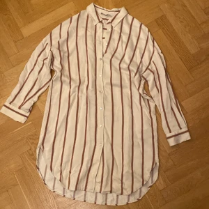 Randig skjorta från Zara - Säljer en stilren randig skjorta från Zara i beige med bruna och grå ränder. Skjortan har långa ärmar och knappar framtill. Perfekt för en avslappnad men ändå snygg look. Kan användas som både en klänning och en skjorta☺️💕