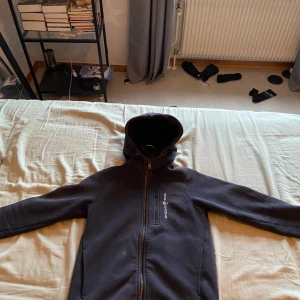 Svart zip hoodie från Sail Racing - Säljer en svart zip hoodie  från Sail Racing med dragkedja och hög krage. Tröjan har långa ärmar och en stilren design. Perfekt för kyligare dagar.  Storlek 150