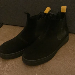 Canada Snow Mount Verm - Snygga svarta boots i mocka från Canada Snow med gul flik på baksidan. Perfekta för höst och vinter med en stilren design och bekväm passform. Skorna är i storlek 42 men de är stora i storleken själv har jag 43
