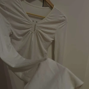 Vit långärmad topp med v-ringning - Säljer en stilren vit långärmad topp med v-ringning och rynkdetalj framtill. Toppen är croppad och har en mjuk och bekväm passform. Perfekt för att matcha med jeans eller kjol.