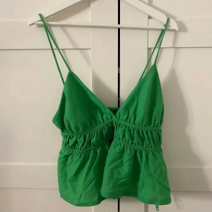 Grön ärmlös topp - Snygg grön ärmlös topp med smala axelband och rynkad midja. Perfekt för varma sommardagar. Enkel och stilren design som passar till många olika outfits.