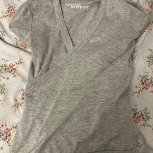 Grå omlottopp från Good Moves -  Grå omlottopp från Good Moves. Toppen har en v-ringning och korta ärmar, perfekt för en avslappnad look. Den är mjuk och bekväm och är i bomull. Toppen är i M men ganska liten i storleken. Om ni har några frågor är det bara att höra av sig, priset kan siskuteras🫶🏼