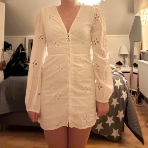 Vit klänning med blommigt mönster - Säljer en söt vit klänning med blommigt broderat mönster. Klänningen har långa ärmar och en v-ringad design med knappar framtill. Perfekt som studentklänning!🙌🏻