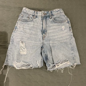 Ljusa jeansshorts med slitningar - Säljer ett par ljusa jeansshorts från H&M (Divided) med coola slitningar och fransiga kanter. De är i storlek 34 i midjan och  har en klassisk femficksdesign samt är högmidjade och perfekta för sommaren. Säljer dessa då de tyvärr inte kommer till användning. Kontakta mig för mer information.🩵