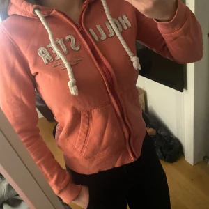 Hoodie från Hollister - Säljer en snygg hoodie från Hollister med dragkedja och justerbar huva. Den är i färgen rosa aprikos. jätte fint skick❣️