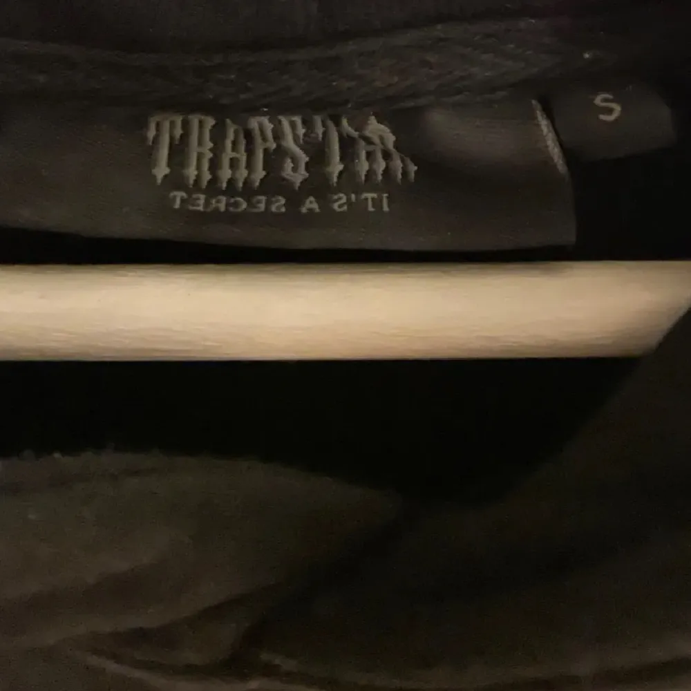 Säljer en svart hoodie från Trapstar med unikt blått och vitt tryck på både fram- och baksidan. . Neuletakit & Villapaidat.