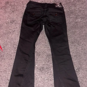 True religion Jeans - Säljer ett par svarta byxor från true religion i bra skick. De har en snygg och stilren design med knappar på bakfickorna. Perfekta för både vardag och fest! OBS byxorna är uppsydda och går inte att sprättas upp. Passar någon som är ca 160cm lång!