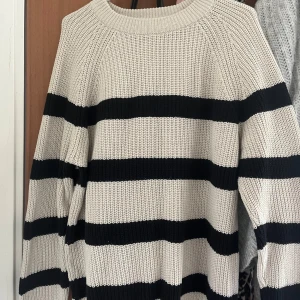 Randig stickad tröja - Säljer en supermysig stickad tröja med breda svarta och vita ränder. Den har en avslappnad passform och långa ärmar, perfekt för kyliga dagar. Tröjan är både stilren och bekväm, ett måste i garderoben!