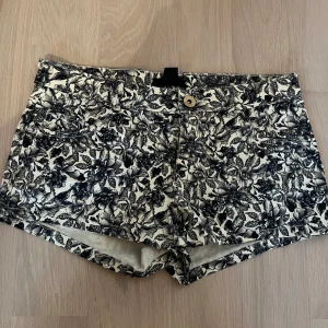 Svartvita blommiga shorts - Säljer ett par snygga och jättecoola lågmidjade shorts med svartvitt blommönster. Jeansshortsen är bara använda ett fåtal gånger. Perfekta för sommaren, till fest, eller nu till hösten med ett par thighs under.