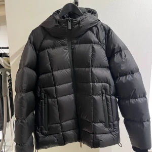 Svart pufferjacka från Dsquared2 - NY VARA!! Säljer en snygg svart pufferjacka från Dsquared2. Den är perfekt för kalla dagar med sin quiltade design och långa ärmar. Jackan har en dragkedja framtill och en stor logga på ryggen. Den är både stilren och varm, perfekt för vintern!