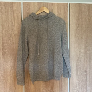 Kashmir hoodie - Säljer en mysig grå hoodie i normal passform. Perfekt för höst och vinter med sin mjuka och varma känsla. Den har en klassisk design med dragsko i huvan och ribbade muddar vid ärmslut och nederkant. Perfekt för chill dagar eller när du bara vill vara bekväm.