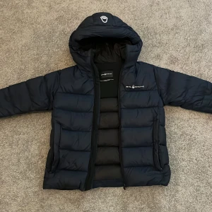 Sailracing Dunjacka       - Nu säljar jag denna marinblåa dunjacka från Sailracing, den är perfekt för sveriges kylliga vintrar och är även vindtät. Den har två ytterfickor samt en på insidan. Jackan är välanvänd men i bra skick och är i storlek 160✅Nypris är 2799kr🙂