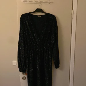 Svart glittrig klänning - Säljer en elegant svart klänning med glittrigt mönster. Den har långa ärmar och en v-ringad design som ger en stilren look. Perfekt för festliga tillfällen som nyår eller jul. Klänningen är i bra skick och passar perfekt för dig som vill glänsa lite extra.