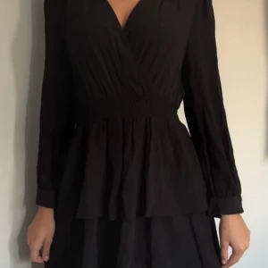 Svart omlottklänning - Snygg svart omlottklänning med långa ärmar och v-ringad hals. Perfekt för både fest och vardag. Den har en smickrande passform med volangdetaljer i nederkant. Klänningen är i ett mjukt och bekvämt material som ger en elegant look. Från Zara i storlek XS