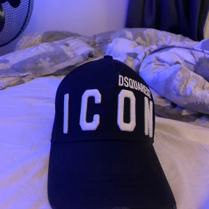 Dsquared2 keps - Säljer en svart keps från Dsquared2 med texten 'ICON' broderad i vitt på framsidan. Kepsen har en justerbar rem baktill och är i bra skick.  Passar de flesta huvudstorlekar. Självklart äkta!