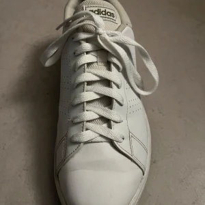 Vita Adidas sneakers - Säljer ett par klassiska vita Adidas sneakers i bra skick. De har en stilren design med snörning och perforerade detaljer på sidorna. Perfekta för vardagsbruk och passar till nästan allt. Skorna är bekväma och har en tidlös look. Perfekta för både vår och sommar! Pris kan diskuteras.