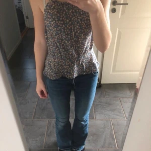 Blommig ärmlös topp - Säljer en söt blommig topp i blått med små blommor i olika färger. Toppen är ärmlös och har smala axelband, perfekt för sommardagar. Den har en luftig passform och är superbekväm att bära. Passar både till jeans och kjol för en avslappnad look💗