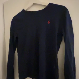 Mörkblå tröja från Polo Ralph Lauren - Säljer en snygg mörkblå tröja från Polo Ralph Lauren i mycket bra skick. Den har en klassisk design med långärmade ärmar och det ikoniska röda logotypbroderiet på bröstet. Perfekt för både vardag och lite finare tillfällen. Passar bra till jeans eller chinos! Den är 160 i barnstorlek och sitter som en XXS/XS.