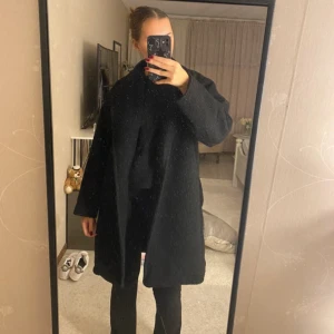 Svart kappa - Säljer en stilren svart kappa i mycket bra skick. Den har långa ärmar och en lös passform, perfekt för höst och vinter. Kappan har ett litet hål i fickan men är ej synligt och går att fixa