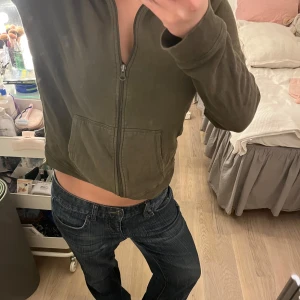 Olivgrön hoodie med dragkedja - Säljer en olivgrön hoodie i ett andvänt men bra skick. Den är croppad och har en dragkedja framtill samt en mysig huva. Perfekt för en avslappnad stil och passar bra till jeans. Storleken är dam S.