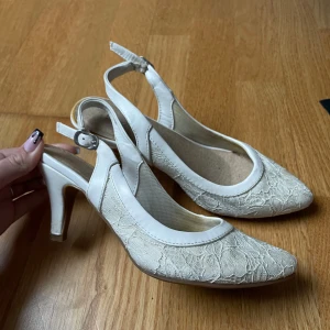 Beige spetsiga pumps med klack - Säljer ett par eleganta beige pumps med spetsig tå och klack. Skorna har en vacker spetsdetalj och justerbar rem runt hälen. Perfekta för festliga tillfällen eller en utekväll. 