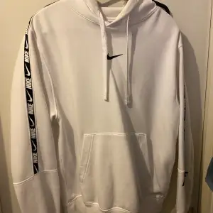 Säljer en snygg vit hoodie från Nike i storlek M. Den har en klassisk design med svarta Nike-loggor längs ärmarna och en känguruficka framtill. Perfekt för både träning och vardag. Huvan har justerbara snören för bästa passform. Superbekväm och stilren! 