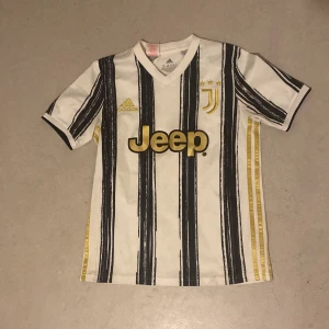 Juventus fotbollströja från Adidas - Säljer en Juventus fotbollströja i vitt med svarta ränder och guldiga detaljer. Tröjan har korta ärmar och är i mycket bra skick. Den har Juventus-loggan och Jeep som sponsor på framsidan. Perfekt för alla fotbollsfans!