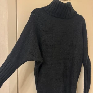 Svart stickad polotröja - Säljer en svart stickad polotröja med en snygg öppen ryggdetalj. Tröjan har långa ärmar och en mysig polokrage, perfekt för kyliga dagar. Den är både stilren och bekväm, idealisk för höst och vinter. Passar bra till både jeans och kjol!