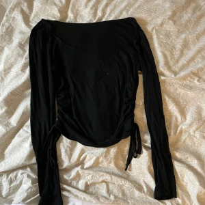 Svart långärmad topp med knyt - Säljer en stilren svart långärmad topp med knyt i sidorna. Perfekt för både vardag och fest! Materialet är mjukt och stretchigt, vilket gör den superbekväm att ha på sig. Passar bra till jeans eller kjol för en snygg look.