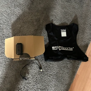 Svart träningsväst från STATSports - Säljer en svart träningsväst från STATSports i mycket bra skick. Perfekt för träning med inbyggd teknologi för att mäta prestation. Västen är tight och bekväm, idealisk för sportaktiviteter. Inkluderar laddningskabel och originalförpackning.