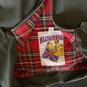 Olivgrön Harringtonjacka med rutig insida - Säljer en klassisk olivgrön Harringtonjacka i storlek M. Jackan har en snygg rutig insida i rött och svart, och stängs med dragkedja. Perfekt för höst och vår! 🧥🍂