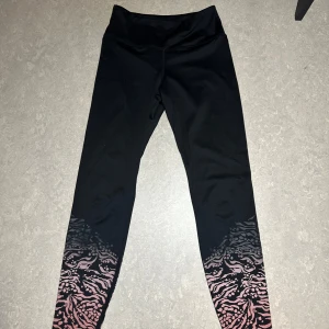 Svarta leggings med rosa mönster - Snygga svarta leggings med ett coolt rosa mönster längst ner. Perfekta för träning eller en avslappnad dag. De är stretchiga och bekväma, vilket gör dem till ett måste i garderoben. Passar bra till både sneakers och träningsskor.