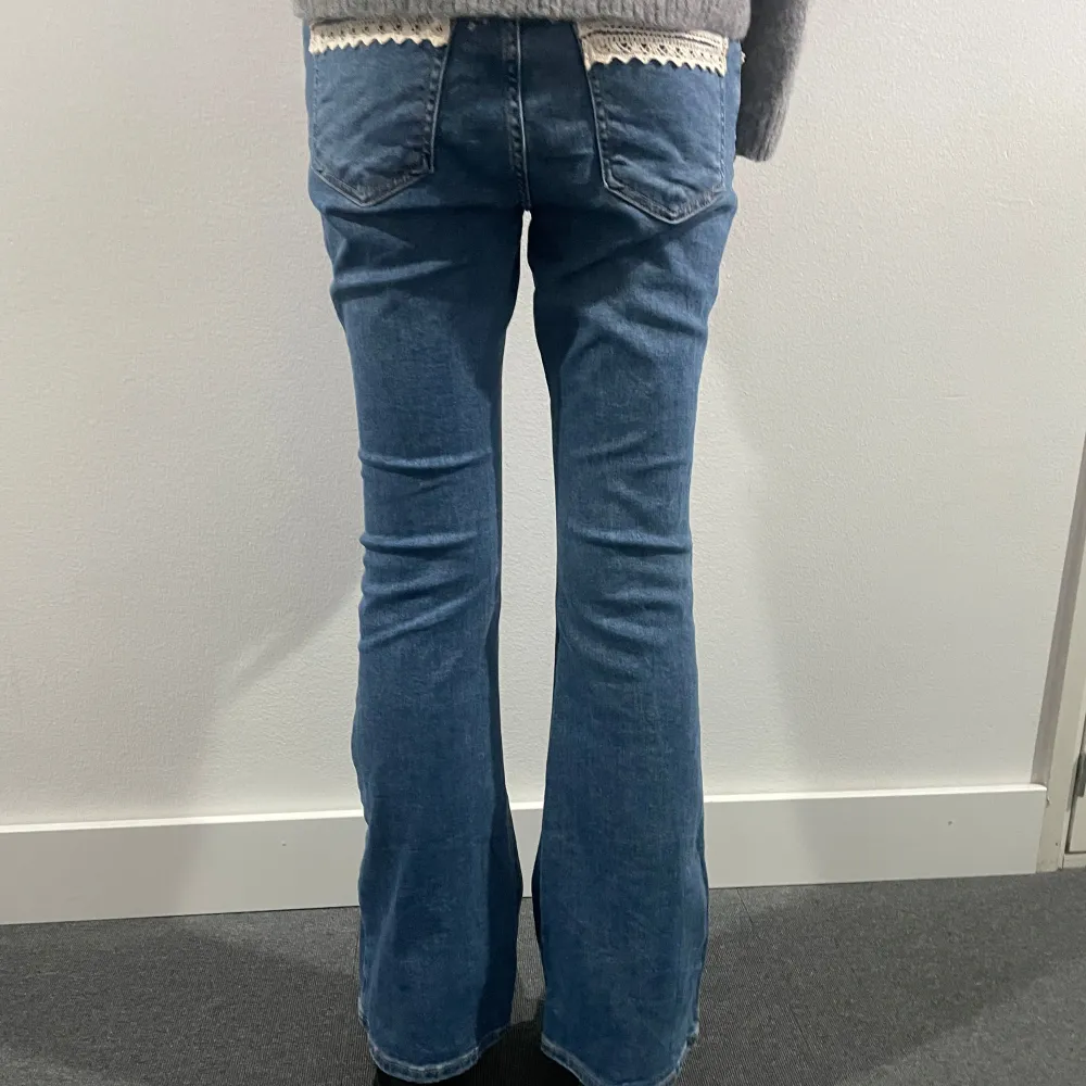 Säljer ett par snygga blå jeans från Gina Tricot. De har unika spetsdetaljer på fickorna både fram och bak, vilket ger dem en söt touch. De är lowaist och bootcut. Storlek: 38. Modellen är 178 cm lång.. Jeans & Byxor.