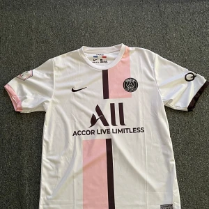 PSG fotbollströja  - Säljer en snygg PSG fotbollströja i vitt med rosa detaljer. Tröjan har korta ärmar och är i mycket bra skick. Den användes säsongen 21/22 och var deras borta tröja. Den är i storlek L men passar lika bra med M 