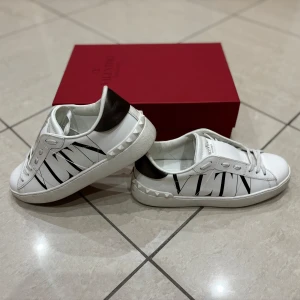Valentino Sneakers  - Säljer ett par snygga Valentino sneakers i vitt med svart VLTN-logga på sidan. Dam storlek 37,5. Bra skick överlag. Box, dustbag samt nya skosnören medföljer. Nypris cirka 6 000. Pris kan diskuteras vid snabb affär. 
