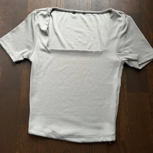 Grå topp med fyrkantig urringning - Snygg grå topp med fyrkantig urringning och korta ärmar. Perfekt för både vardag och fest. Materialet känns mjukt och bekvämt mot huden. 