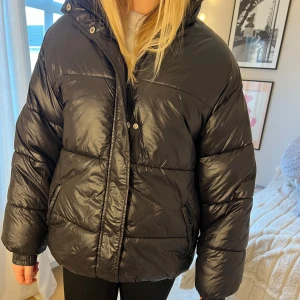 Svart pufferjacka - Säljer en svart pufferjacka i mycket bra skick. Den är perfekt för kalla vinterdagar och har en skön, vadderad känsla. Jackan har långa ärmar och stängs med dragkedja och knappar. Den är både snygg och praktisk för vintern! Den är i storleken xxs men är stor i storleken