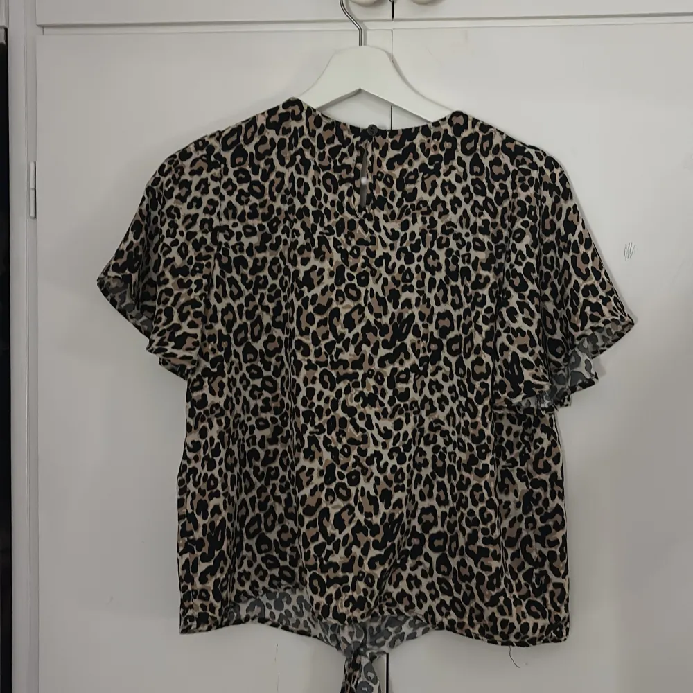 Säljer en cool leopardmönstrad topp från Lindex i storlek 164. Toppen har korta ärmar och en knytning framtill som ger en trendig look. Perfekt för både vardag och fest! 🐆. Yläosat.