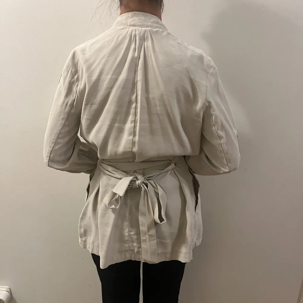 Säljer en stilren beige kavaj med knytband i midjan. Den har trekvartsärmar och en lös passform som ger en avslappnad look. Perfekt för vår och sommar, och funkar både till vardags och fest. Kavajen är i mycket bra skick och är superbekväm att ha på sig.. Neuletakit & Villapaidat.
