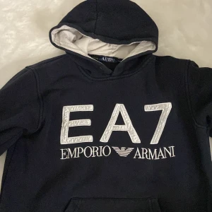 Svart hoodie från Emporio Armani - Säljer en snygg svart hoodie från Emporio Armani med stort EA7-tryck på framsidan. Den har en klassisk design med huva och är perfekt för både vardag och chill. Superbekväm och stilren, passar till allt! 🖤
