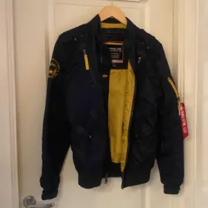 Säljer en snygg mörkblå bomberjacka från Alpha Industries. Den har en gul insida och coola detaljer som dragkedjor och en ficka på ärmen. Perfekt för höst och vår! Jackan är i mycket bra skick och passar till alla tillfällen.