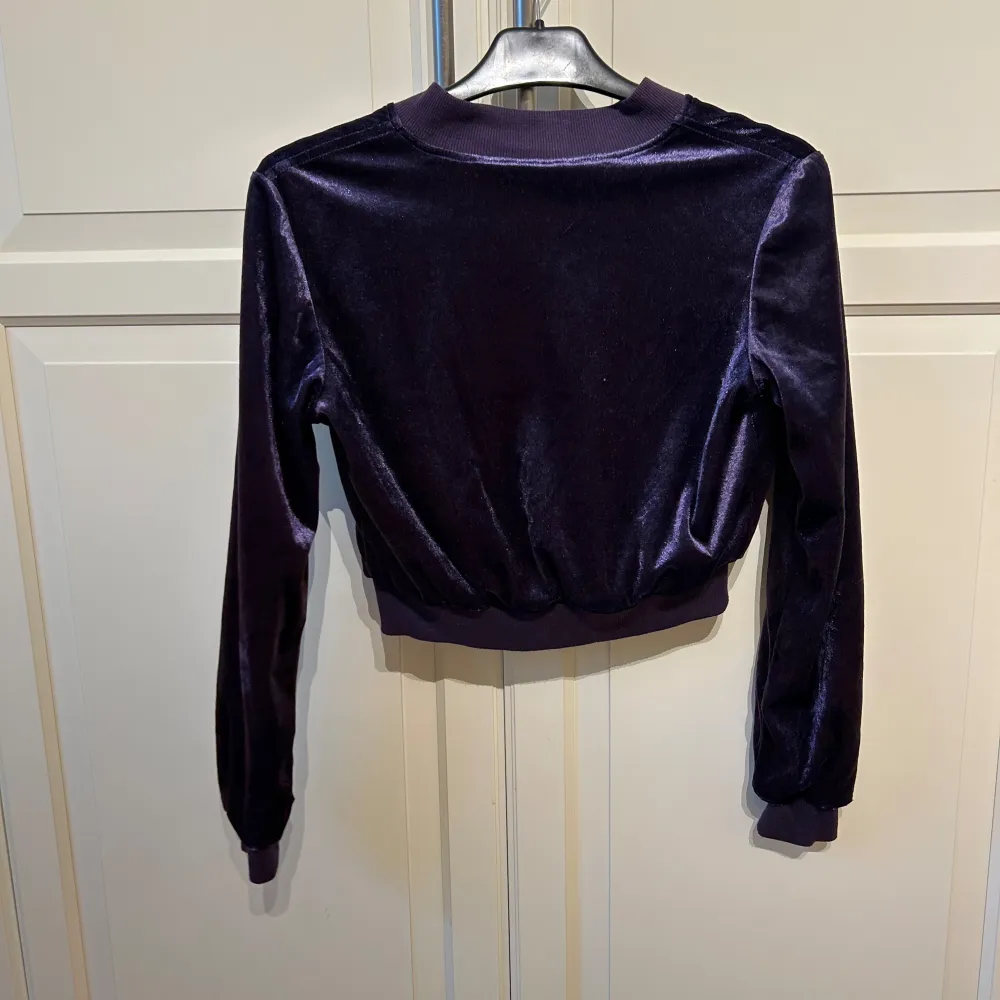 Superfin mörklila velourjacka från Gina Tricot. Den är croppad med dragkedja och har långa ärmar. Jackan har två fickor med dragkedjor framtill. . Takit.