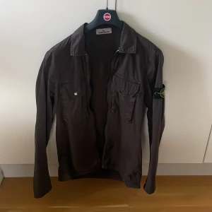 Stone Island Overshirt - Säljer en snygg brun overshirt från Stone Island. Den har två bröstfickor med knappar. Klassisk Stone Island-logga på ärmen. Overshirten är i nyskick då den aldrig har använts. Hör av dig vid funderingar // Olle 