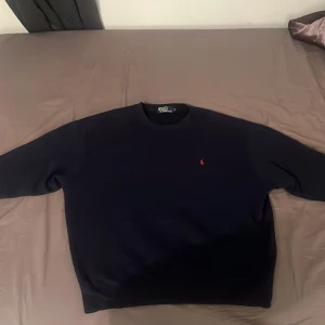 Mörk blå tröja från Polo Ralph Lauren - Säljer en klassisk svart tröja från Polo Ralph Lauren i storlek M. Den har en röd broderad logga på bröstet och är perfekt för både vardag och fest. Tröjan är i mycket bra skick och passar till alla säsonger. Skön och stilren design!