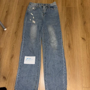 Blå jeans med slitningar - Säljer ett par snygga blå jeans med slitningar på framsidan. De har en klassisk femficksdesign och en bekväm passform. Perfekta för en avslappnad stil och kan matchas med nästan vad som helst. Passar både till vardags och fest!
