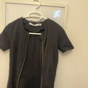 Svart klänning från & Other Stories - Snygg svart klänning från & Other Stories i storlek S. Den har en stilren design med korta ärmar och en dragkedja framtill. Perfekt för både vardag och fest!