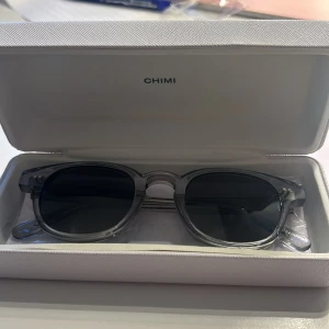 Grå solglasögon från Chimi - Säljer ett par snygga grå solglasögon från Chimi. De kommer i ett stilrent fodral med Chimi-loggan. Perfekta för att ge din outfit en cool touch. Glasögonen har en rund form och är i nyskick. Perfekta för både vardag och fest💕💕