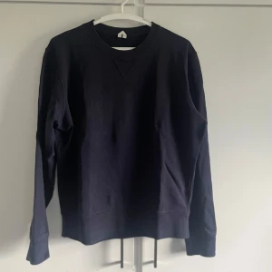 Svart sweatshirt i bomull - Säljer en marinblå sweatshirt i bomull från arket. Den är enkel och stilren med rund hals och långa ärmar. Perfekt för en avslappnad look. Lite använd men i bra skick. Lite urtvättad och sen ett liten hål på magen, se bild. Nypris 450kr
