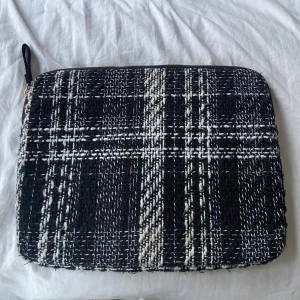 Rutig datorväska med dragkedja - Säljer en snygg rutig datorväska i svart och vit. Den har en praktisk dragkedja och är perfekt för att skydda din laptop. Väskan har en stilren design med ett klassiskt rutmönster.