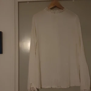 Vit blus med spetsdetaljer - Säljer en elegant vit blus med vackra spetsdetaljer vid halsen och ärmsluten.